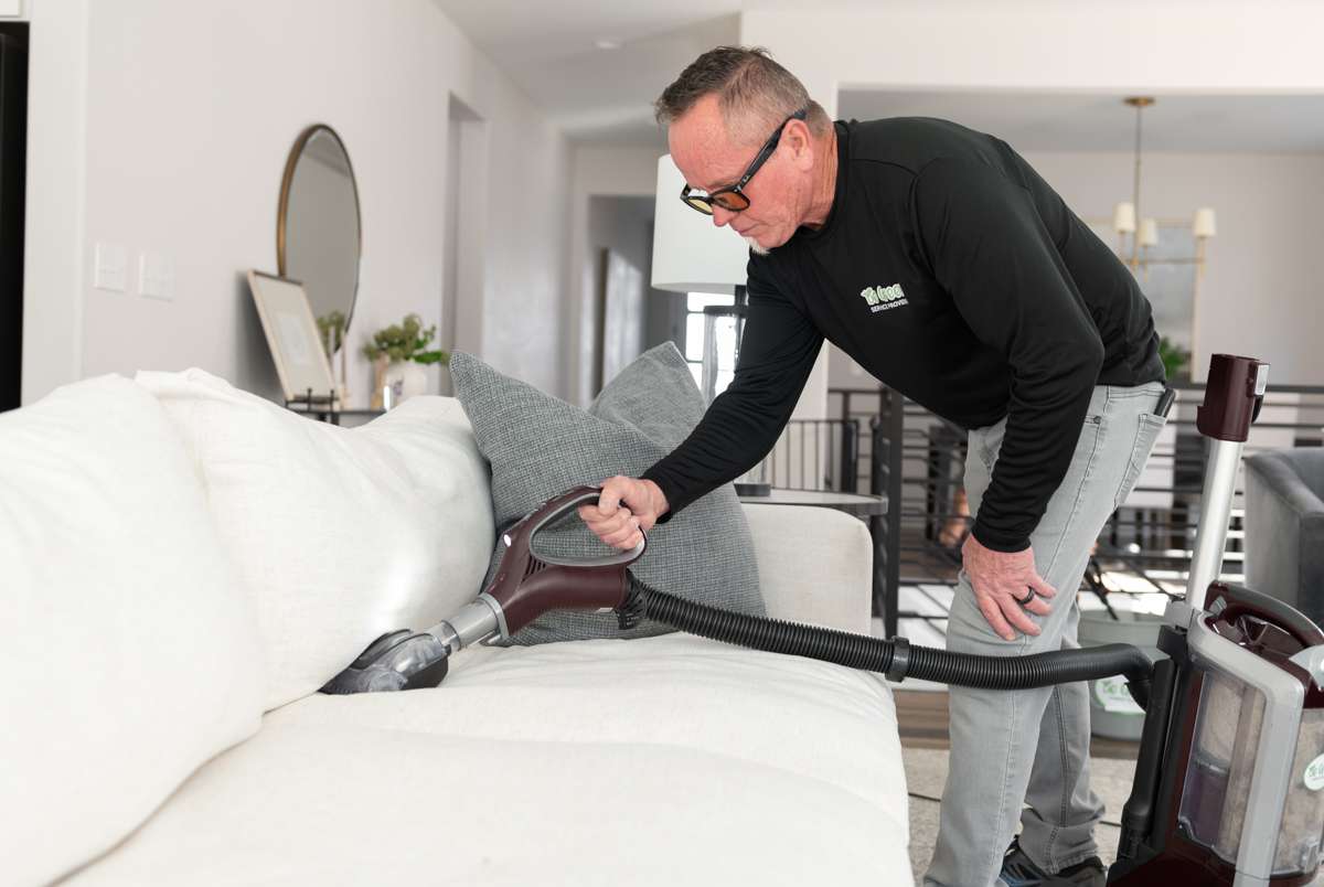 Professional green carpet cleaner vacuum's a white sofa.