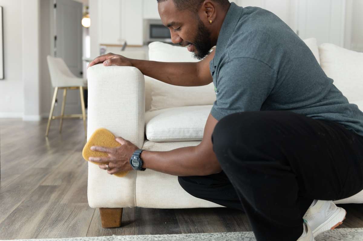 Professional carpet cleaner using a sponge to clean a white couch with natural cleaning chemicals.