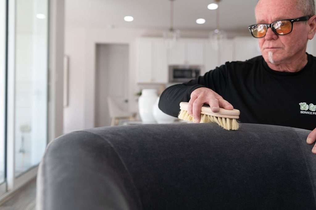 Professional carpet cleaner uses a natural fiber brush to clean upholstery